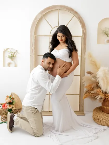 A tender moment between partners, listening to the baby's first flutters. This maternity couple portrait, set against a bright and airy backdrop, beautifully captures the shared excitement of expecting parents.