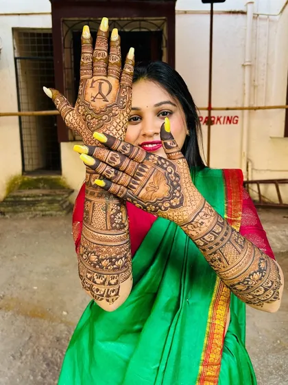 A happy bride posing with her full bridal mehndi, which features her and her partner's initials.