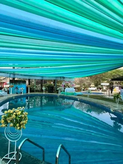 A full view of a stunning poolside setup, where we used long, flowing drapes in shades of blue and green over the pool. This creates a spectacular visual effect and provides shade for a daytime event.
