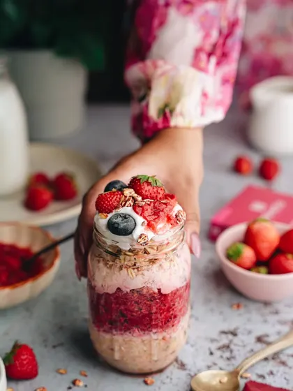 A lifestyle shot for a health food brand, featuring a hand holding a jar of strawberry overnight oats. This type of image helps customers connect with the product on a personal level.
