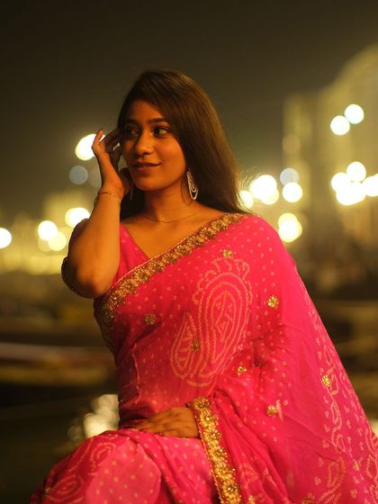 A candid moment of beauty and grace, with the festive lights of Dev Deepawali reflecting on the Ganga in the background.