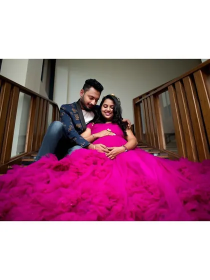A fun and sweet indoor maternity photo. The vibrant magenta ruffled gown fills the frame with color and joy.