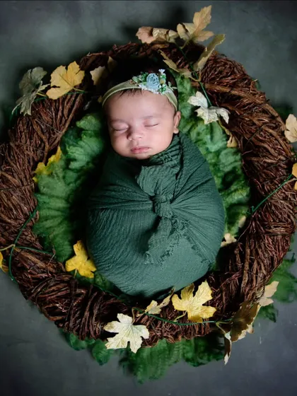 I love using natural elements in my newborn photography. Here, a baby is wrapped in a deep green swaddle, nestled inside a rustic wreath of autumn leaves for an earthy, organic feel.