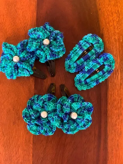 A set of floral hair clips in rich shades of teal and blue. The pearl center adds a classic touch to these handmade crochet accessories.