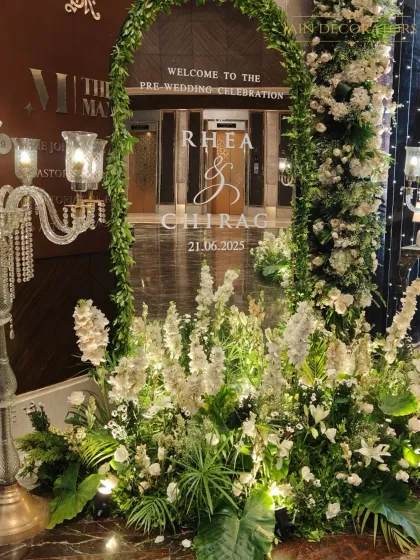 A personalized welcome for a pre-wedding celebration. The elegant sign is framed by an arch of lush white flowers and greenery, setting a sophisticated and romantic tone.