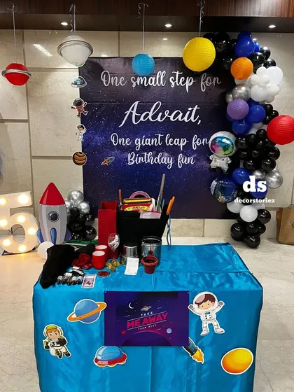 A detailed look at the space-themed party table, featuring astronaut and planet cutouts, a 'Take Away' sign for party favors, and a large light-up number '5'.