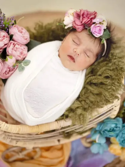 A sweet 22-day-old baby girl sleeping peacefully in a carry cart. The arrangement of soft flowers around her adds a dreamy, delicate touch to this newborn portrait.