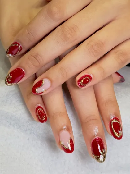 Getting into the festive spirit with this elegant red and gold nail art. This design features a rich red base with intricate gold 3D accents and negative space details, perfect for any celebration.