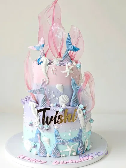 An underwater fantasy, this two-tier mermaid cake is decorated in pastel shades of pink, purple, and blue. It features mermaid tails, seahorses, and delicate rice paper sails for a dreamy, oceanic feel.