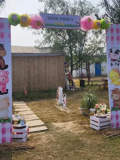 A welcoming entrance arch for the farm party. The pillars are decorated with a pink gingham pattern and stacked animal illustrations, creating a cute and inviting entryway.