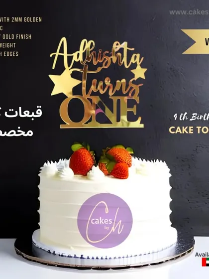 A mockup of the "Adrishta turns ONE" topper in gold on a simple white cake with strawberries.