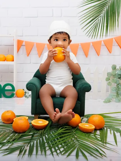A one-year-old girl curiously inspects an orange during her fruit-themed milestone session.