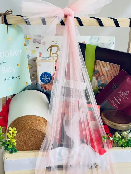Welcoming a new life is a joyous occasion, and this baby shower hamper is designed to match. Packed in a beautiful pinewood basket, it includes essentials from The Moms Co., a personalized photo frame, and sweet treats for the parents-to-be.