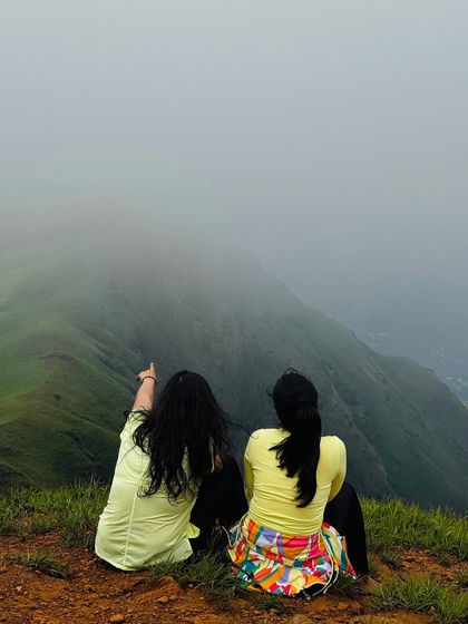 Two friends sit at the edge of the Netravati peak, pointing towards the sea of clouds below. A perfect moment of shared wonder.