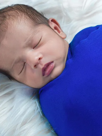 A close-up of a newborn wrapped snugly in a vibrant blue cloth. This angle highlights the baby's perfect profile and soft hair.