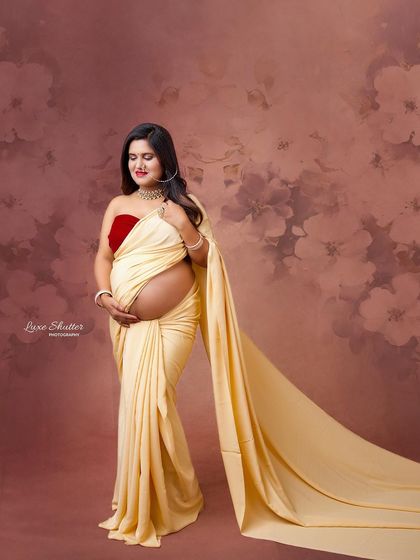 This bare-bump saree drape is a beautiful way to celebrate the female form during pregnancy. The soft, painterly background adds a touch of artistic elegance.