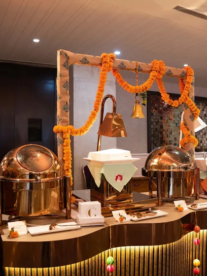 A traditional buffet station adorned with marigold garlands and brass bells. The gleaming copper chafing dishes add a touch of royalty to the setup, reflecting our commitment to heritage.