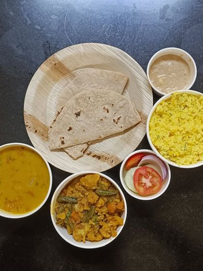 A single trial meal, plated to show the portion size. It includes lemon rice, mix veg sabzi, dal, rotis, salad, and a side of chutney.