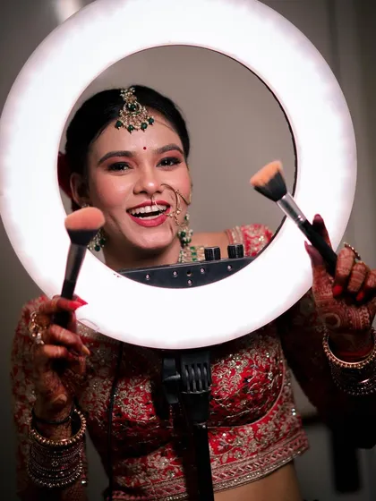 A fun and playful bridal portrait where the bride smiles brightly while posing with a ring light and makeup brushes. This shot captures her joyful personality and the excitement of getting ready.
