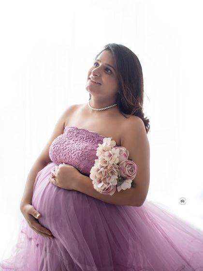 A beautiful high-key portrait of an expecting mother in a lavender gown, looking up with a hopeful smile. This style creates a bright and airy feel.
