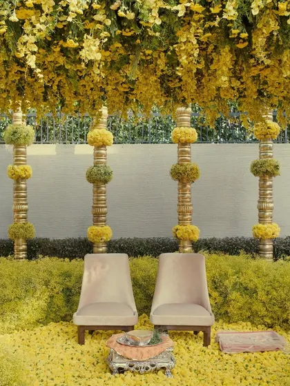 The seating for a Haldi ceremony, set against a backdrop of golden pillars wrapped in floral spheres. The entire area is a celebration of yellow, symbolizing happiness and new beginnings.