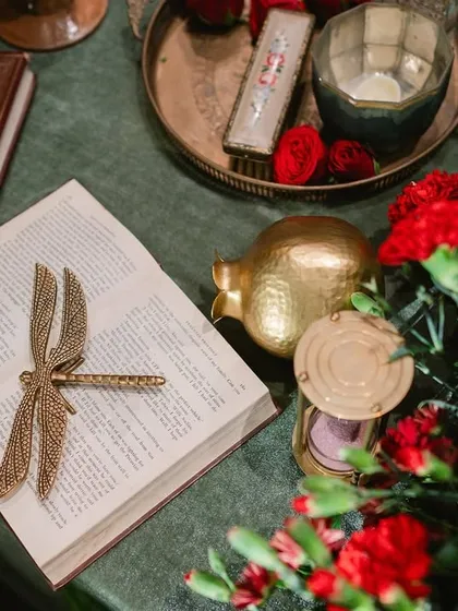 It's the personal details that tell the real story. For an art-themed sangeet, we curated objects like this brass dragonfly bookmark, vintage books, and golden pomegranates to evoke the feeling of a Raja Ravi Varma still life.