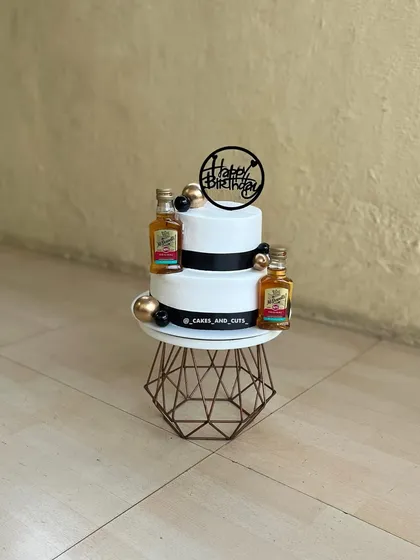 A sophisticated two-tier cake with mini liquor bottles, perfect for a man's birthday celebration. The black, white, and gold theme adds a touch of class.
