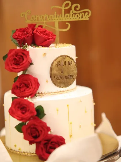 A two-tiered "Congratulations" cake adorned with red roses and a personalized plaque for the couple, Aradhna & Shashank.