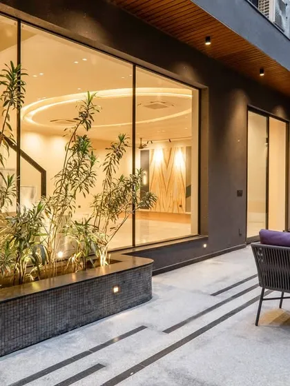 An outdoor sitting area that seamlessly connects with the interior through large glass sliding doors. The design uses planters and strategic lighting to create a cozy and inviting atmosphere for the evenings.