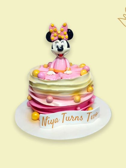 A cute Minnie Mouse cake for a second birthday. The design features a pink and yellow ombre effect, colorful balls, and a personalized banner for the birthday girl.