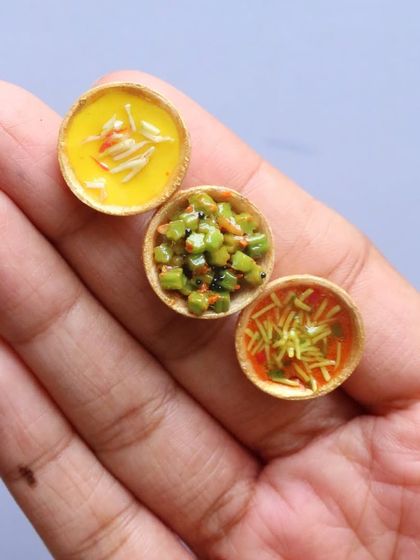 Three tiny bowls of Kathiawadi curries held in the palm of a hand, showcasing their minuscule size.