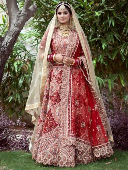 A full view of the stunning red bridal lehenga with peacock embroidery, shot outdoors to show its true color and detail. This is a popular rental choice for brides wanting a traditional yet standout look.