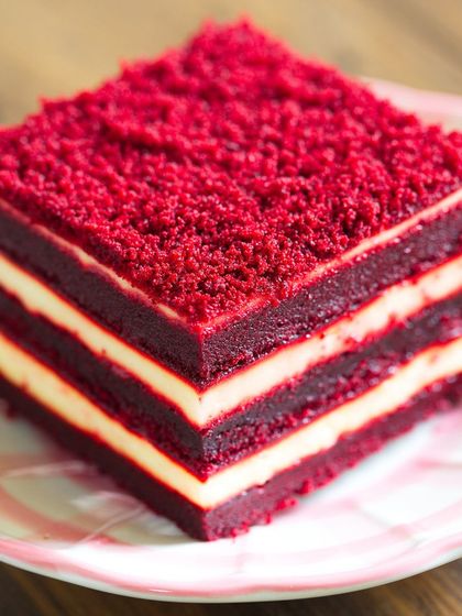 A perfect slice of our layered red velvet cake. This image shows the rich red sponge and the smooth cream cheese frosting layers, giving you a preview of the delicious texture and taste.