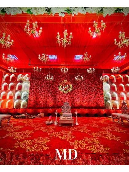 The central seating for the couple at their engagement ceremony. The ornate silver chairs are placed on a stage covered with a royal red and gold patterned carpet, perfectly matching the 'Laal Ishq' theme.