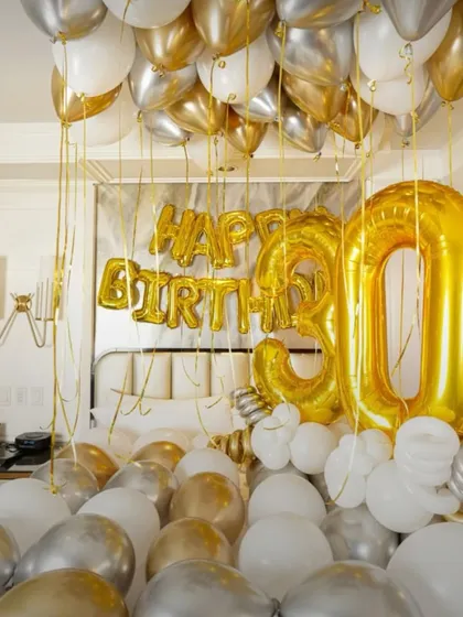 A lavish 30th birthday setup with the bed covered in gold, silver, and white balloons, creating a luxurious and celebratory feel.