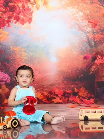 A baby boy plays with wooden toys against a magical, autumn-colored forest backdrop. The warm, glowing light and vibrant red leaves create an enchanting and beautiful atmosphere.
