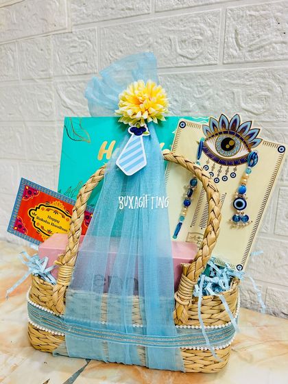 A premium Rakhi hamper for a brother and sister-in-law, featuring an evil eye rakhi set, makeup, and dry fruits in a stylish grass basket.