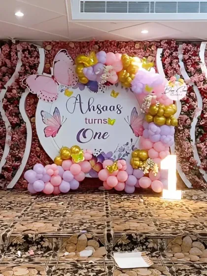 A butterfly-themed stage decoration with a partial balloon arch against a floral backdrop.