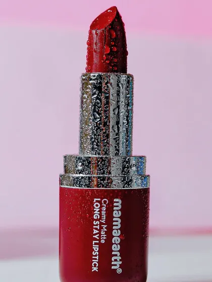 A detailed macro shot of a red Mamaearth lipstick, focusing on the texture of the lipstick and the water droplets on its silver casing.