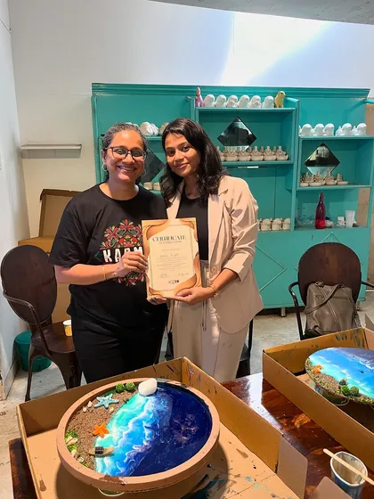 This participant created an incredible ocean-themed resin art piece, complete with sand and shells. She proudly holds her certificate of completion.