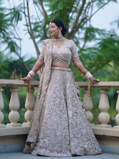 A full-length portrait of a bride on a balcony, showcasing her beautiful muted gold lehenga.