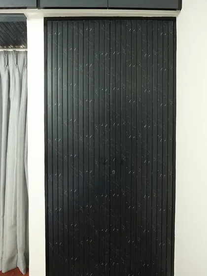 A close-up of the charcoal louvered wardrobe doors, which add a strong textural element to the rustic bedroom design.