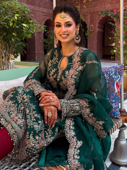 The full mehendi look, showing the client seated and looking radiant. The makeup perfectly complements her green and red outfit.
