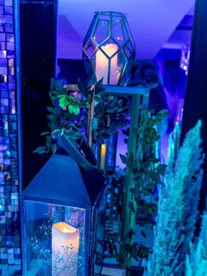 Atmospheric lighting details for a cocktail party. Geometric lanterns with candles inside are placed among greenery, creating a moody and enchanting glow.