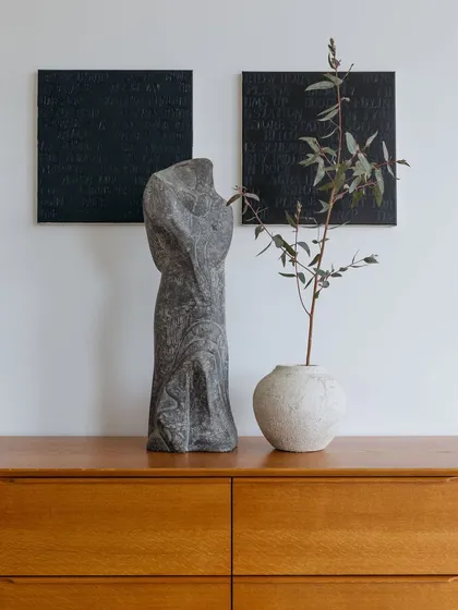 We believe in the harmony of vintage and contemporary styles. Here, a minimalist wooden console provides a stage for a play of textures, featuring a stone sculpture by Piet Van Stuivenberg and a simple, natural branch.