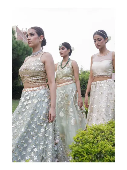 Three models posing in a garden setting, each wearing a different pastel-colored, floral-embroidered lehenga. This photo is perfect for a spring or summer collection, showcasing variety within a single theme.