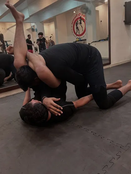 A student applies a triangle choke, using his legs to control his opponent's posture and secure the submission. This is a classic BJJ technique.