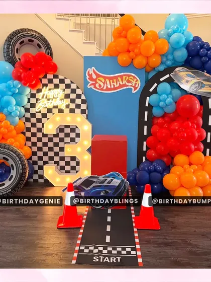 A high-octane Hot Wheels party for a third birthday. The setup includes a racetrack, traffic cones, a light-up number '3', and a vibrant balloon arrangement.