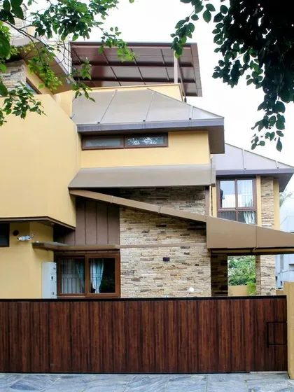 A full view of the home's facade, showing the interplay of different volumes, sloped roofs, and materials. The large wooden gate provides a warm and secure entrance.