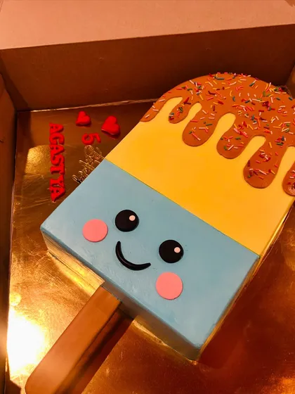 A fun and whimsical cake shaped like a giant, smiling ice cream popsicle with colorful sprinkles.